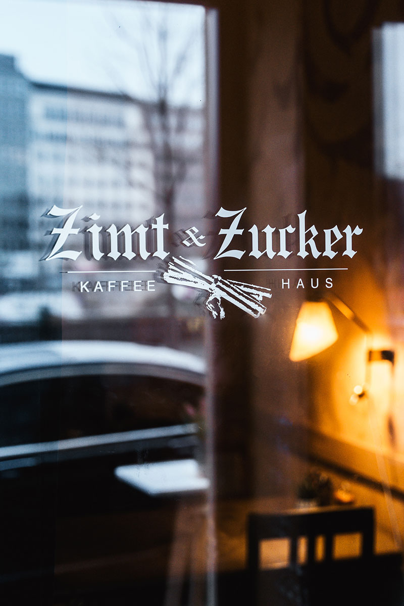 Schaufenster mit Zimt & Zucker Logo darauf. Im Ladeninneren scheint warm eine Lampe.